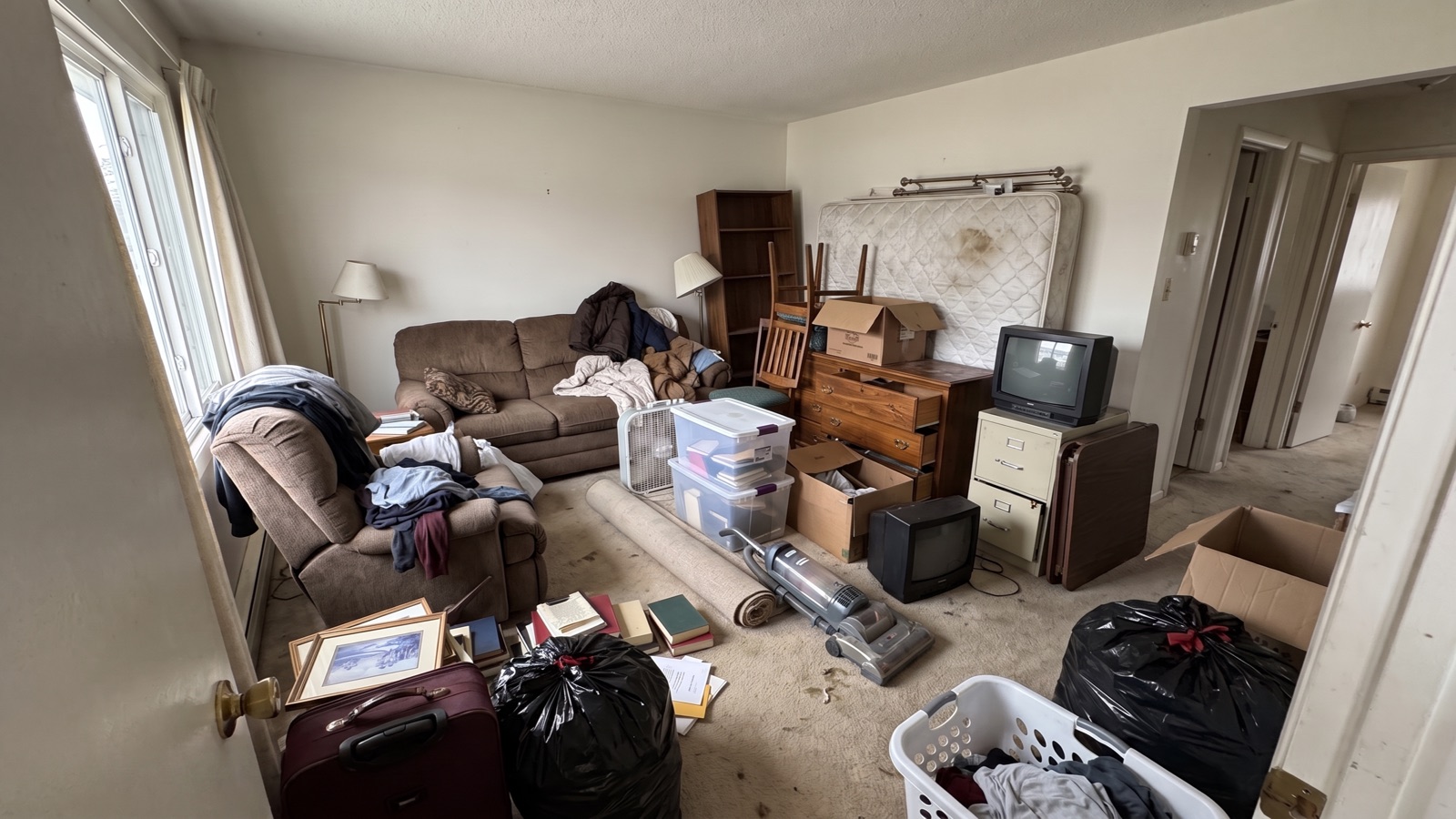 A living room packed with furniture, boxes, bags and a mattress before the haul